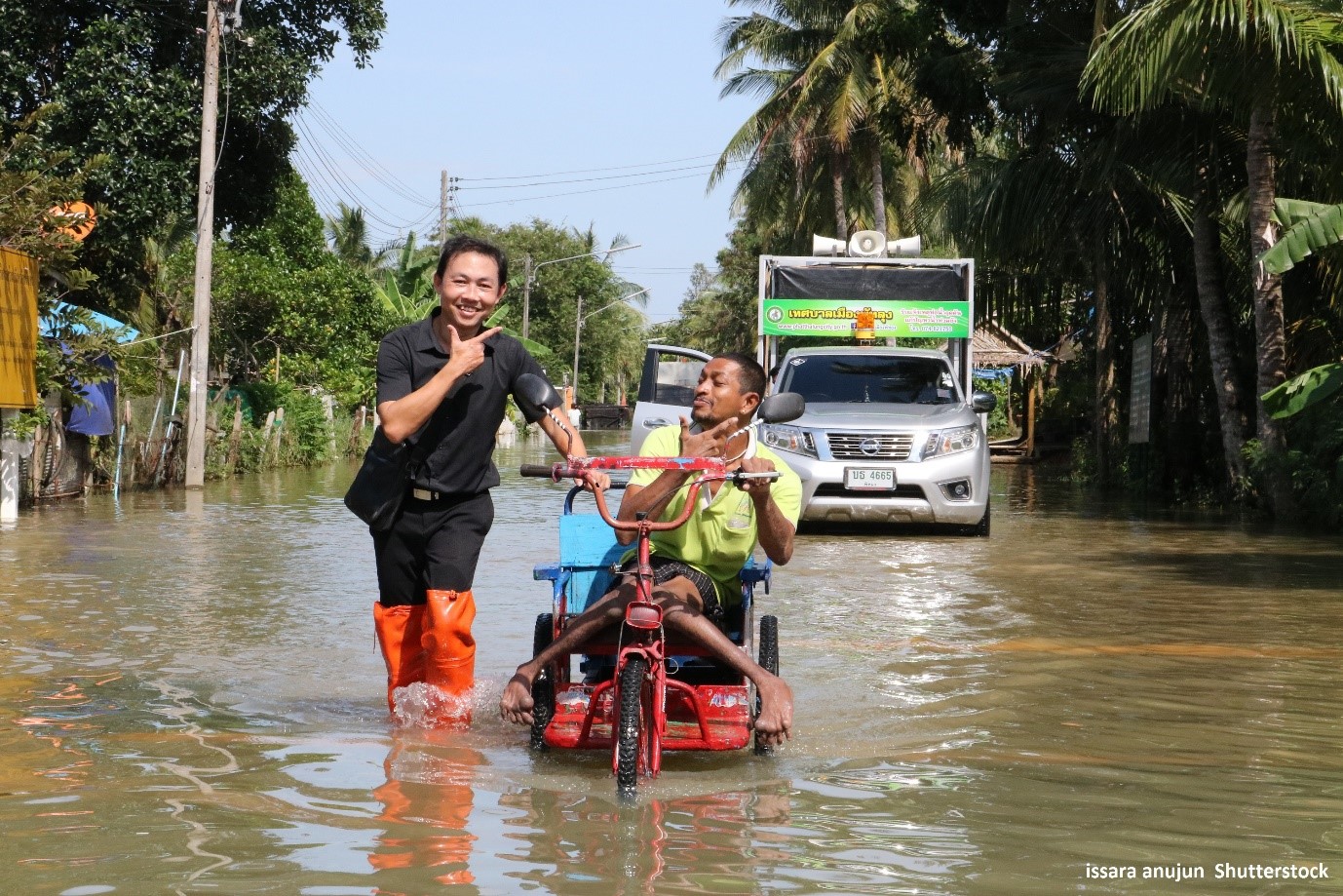 A volunteer in Southern Thailand helps a man with a disability get through a flood in his wheelchair.