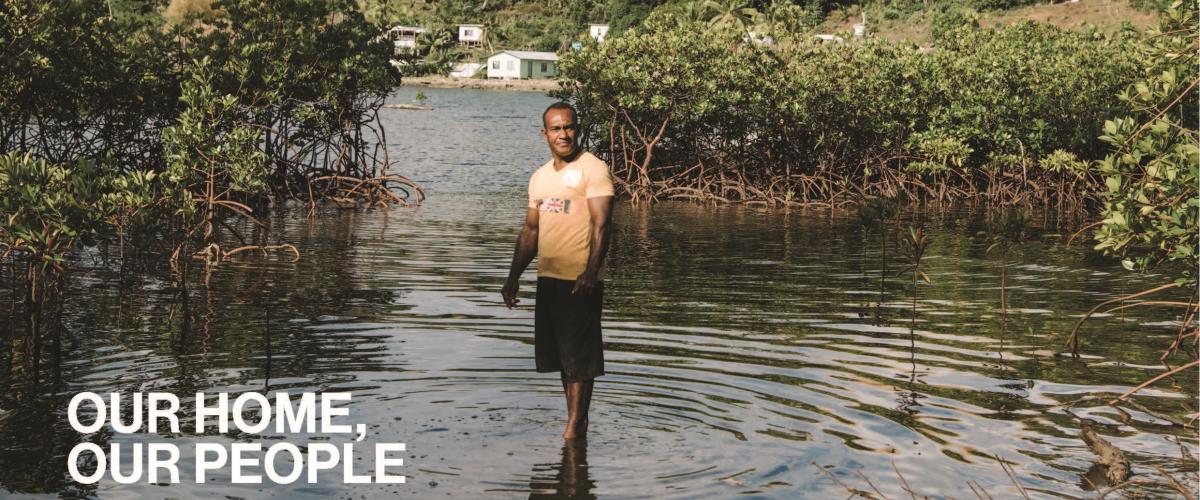 A man in a bright orange shirt stands in the middle of a flooded field