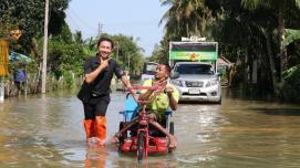 A volunteer in Southern Thailand helps a man with a disability get through a flood in his wheelchair.